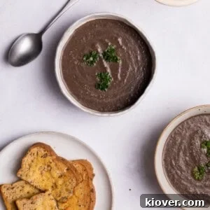 A bowl of creamy vegan mushroom soup garnished with fresh herbs and served with crusty bread on the side.