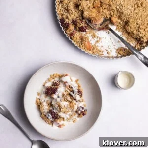 A serving of warm apple and blackberry crumble on a marble background, topped with a dollop of cream.