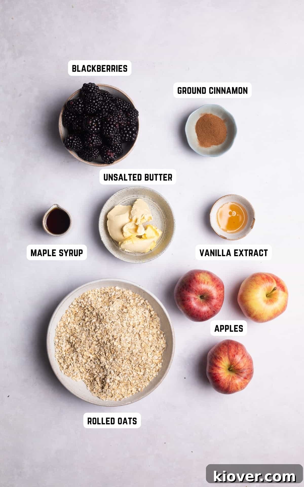 A flat lay photograph showcasing all the fresh ingredients required to make a delicious Apple and Blackberry Crumble, including apples, blackberries, maple syrup, cinnamon, and vanilla.