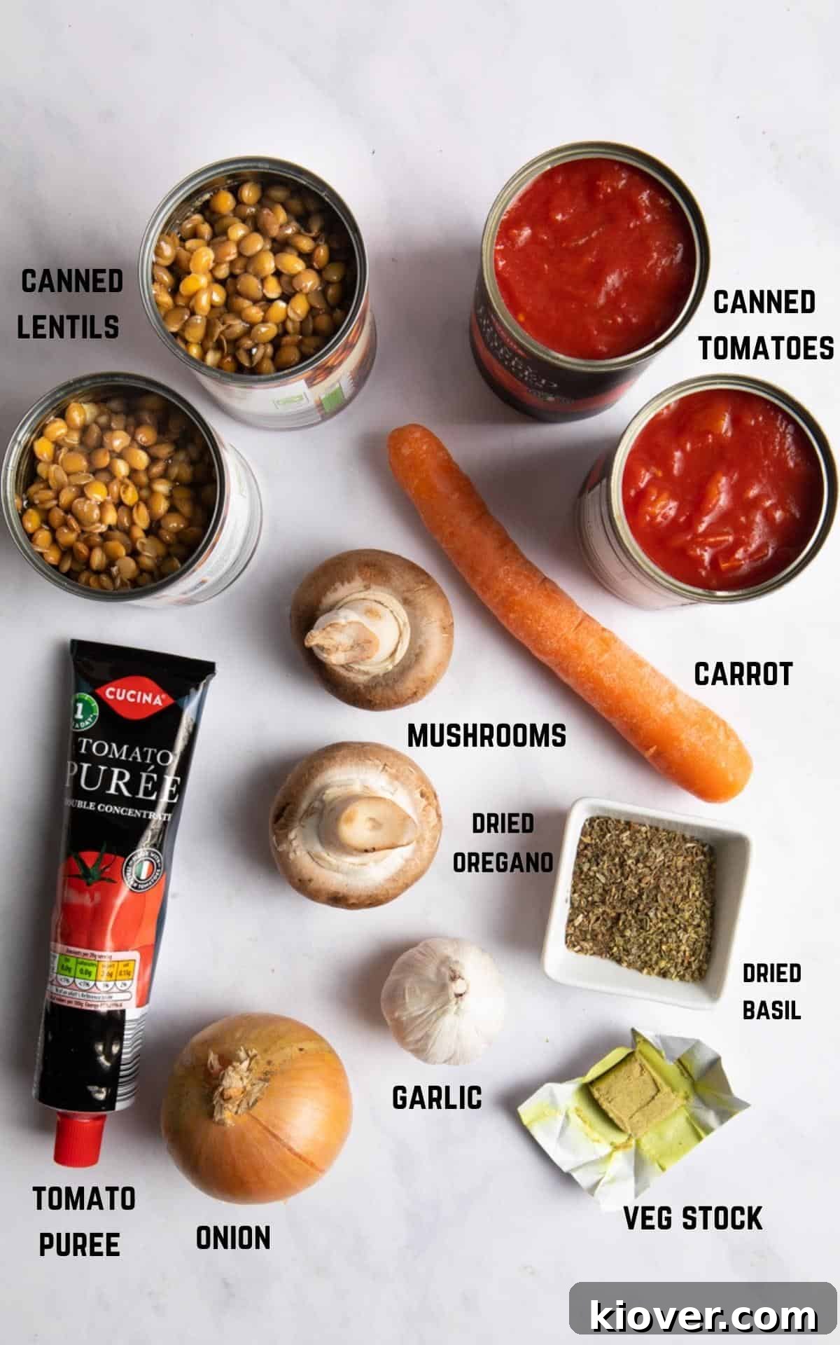 Arrangement of 20-minute lentil bolognese ingredients, including chopped vegetables, herbs, canned goods, and pasta, on a marble background.