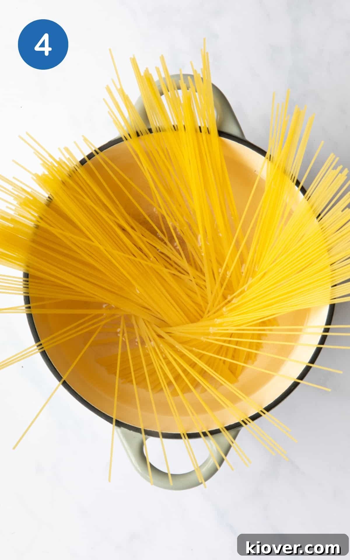 Pasta cooking in a saucepan on a stove, set against a white marble background.