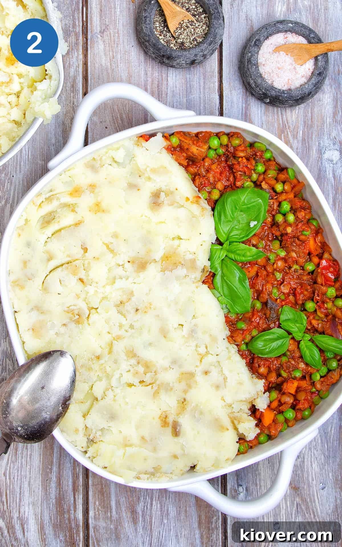 A deep baking dish filled with the rich Vegan Shepherd's Pie base, generously topped with fluffy mashed potatoes, ready for baking.