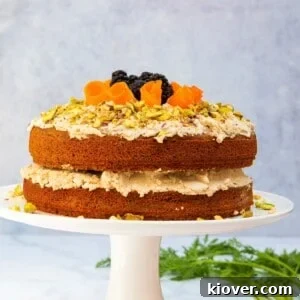 Beautiful vegan carrot cake on a white cake stand against a grey marbled background.
