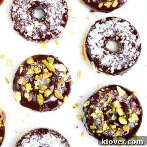 Four delicious vegan homemade doughnuts on a white marble background, topped with pistachio and coconut.