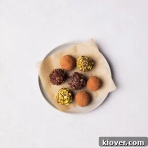 Assortment of vegan chocolate truffles on a plate, dusted with various toppings like cocoa and nuts.