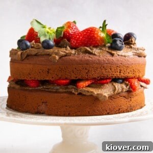 Chocolate cake topped with fresh berries on cream cake stand and white background.