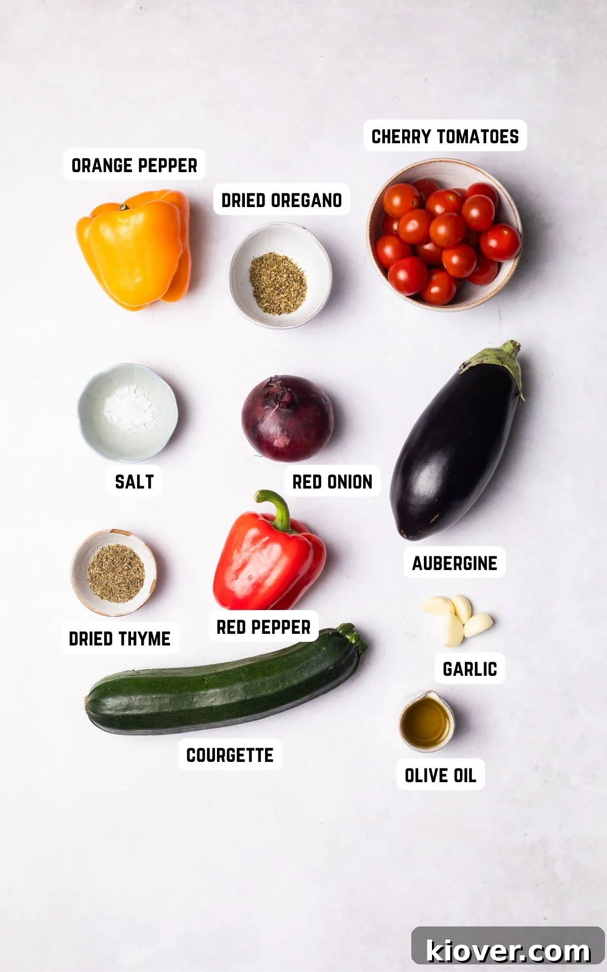 Fresh ingredients laid out for making Mediterranean Vegetables: olive oil, garlic, dried herbs, salt, red onion, red pepper, orange pepper, courgette, aubergine, and cherry tomatoes.