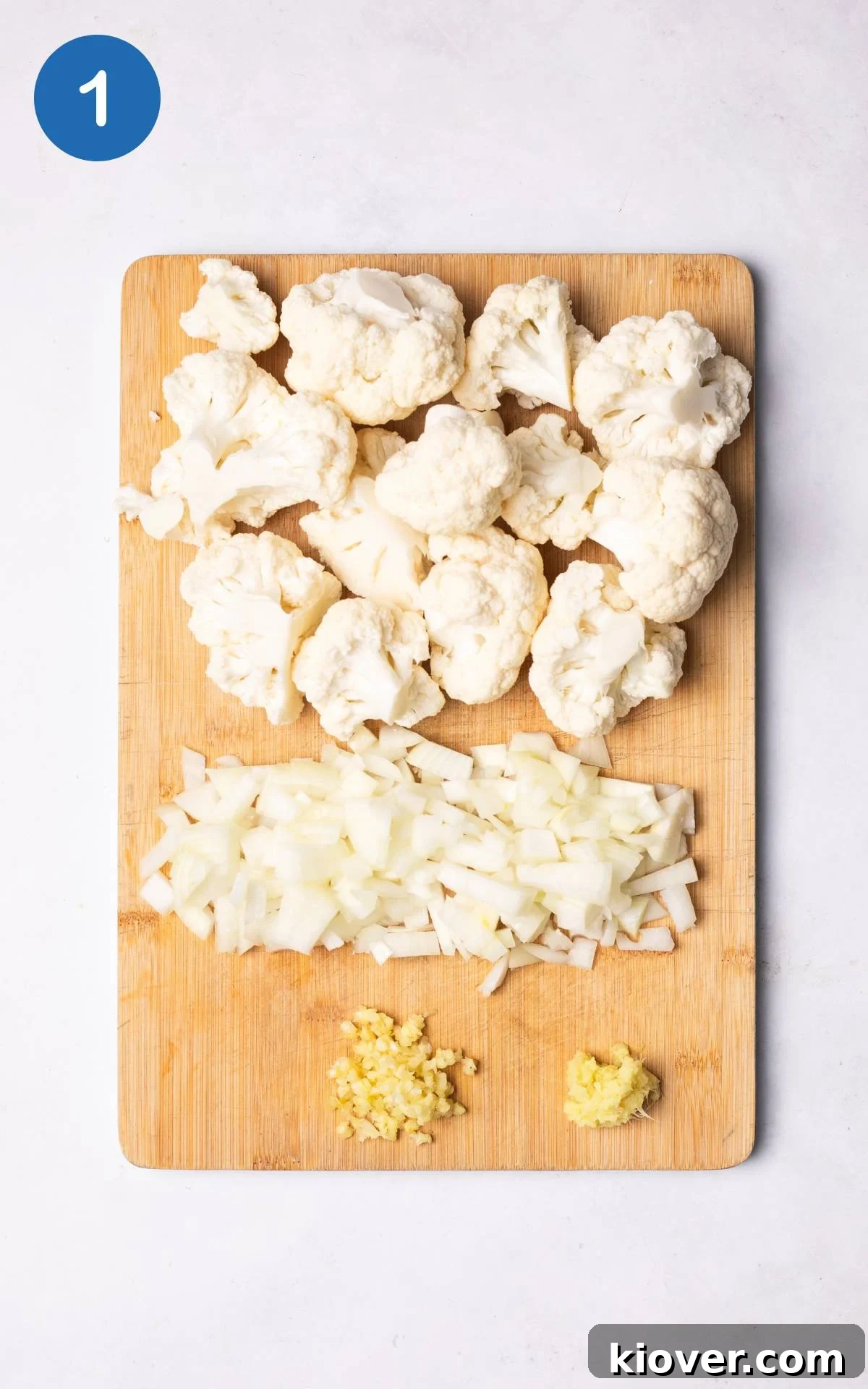 Creamy Cauliflower Delight 4 Diced onion, crushed garlic, grated ginger, and cauliflower florets on a wooden cutting board, ready for cooking.