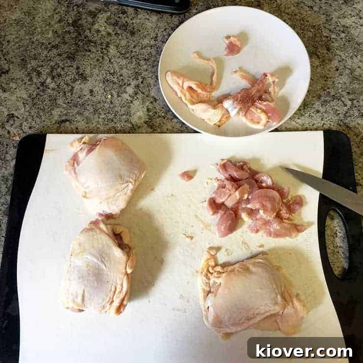 Four raw chicken thighs on a cutting board. One is meticulously cleaned, deboned, and expertly chopped into bite-sized pieces, ready for cooking. The remaining three thighs are whole, awaiting preparation.