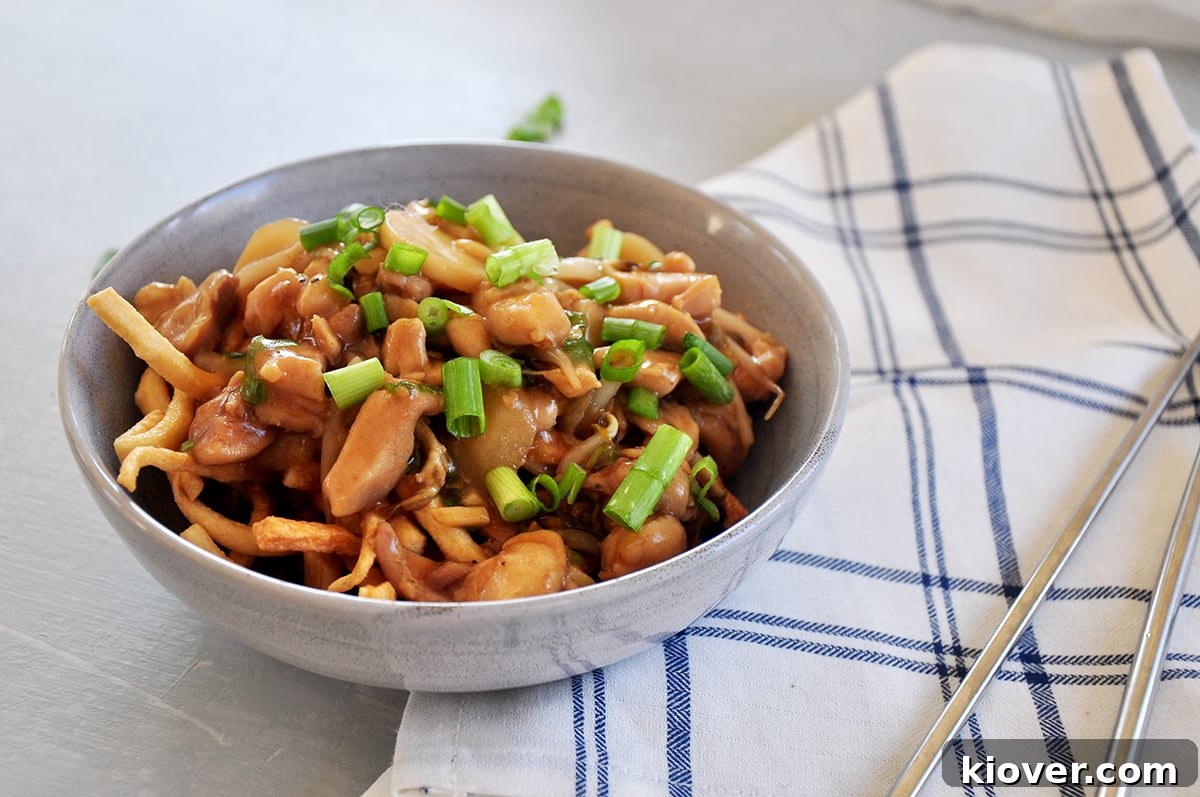 A tantalizing side view of finished crispy chicken chow mein, beautifully plated on a plaid napkin, with chopsticks poised nearby, highlighting its rich textures and inviting aroma.