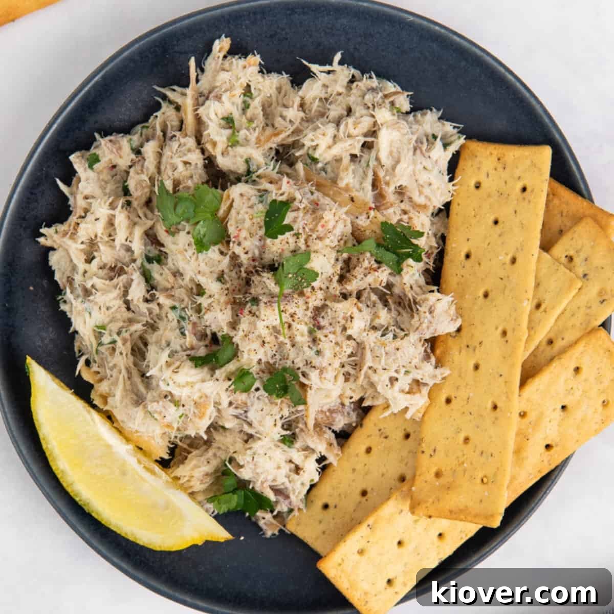 Smoked mackerel pate served beautifully on a blue plate with an assortment of crackers and a wedge of lemon.