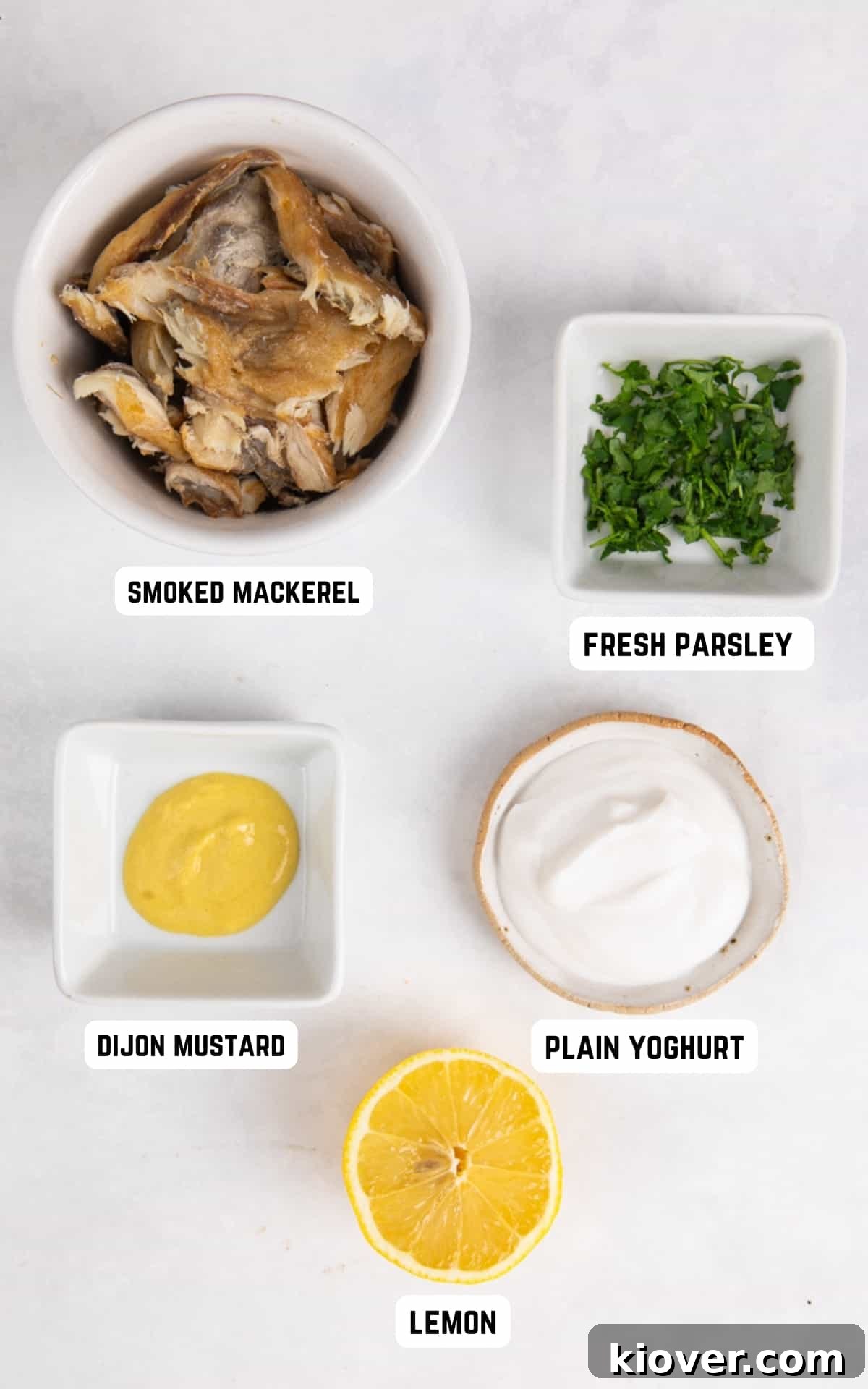 All five ingredients for smoked mackerel pate arranged on a wooden board: smoked mackerel fillets, plain yogurt, Dijon mustard, fresh parsley, and a lemon.