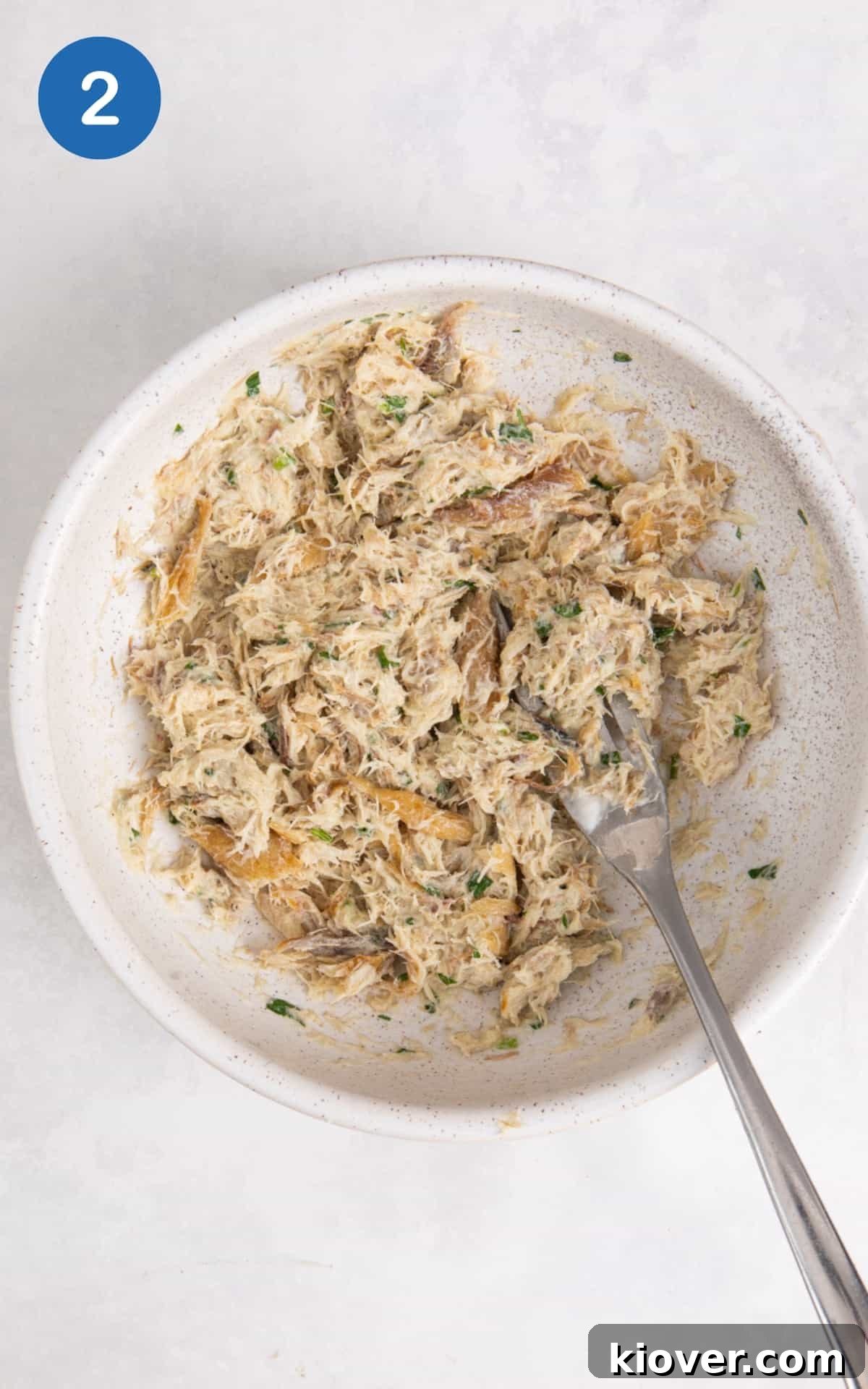 Smoked mackerel pate being mashed together with a fork in a white bowl, showing a creamy, chunky texture.