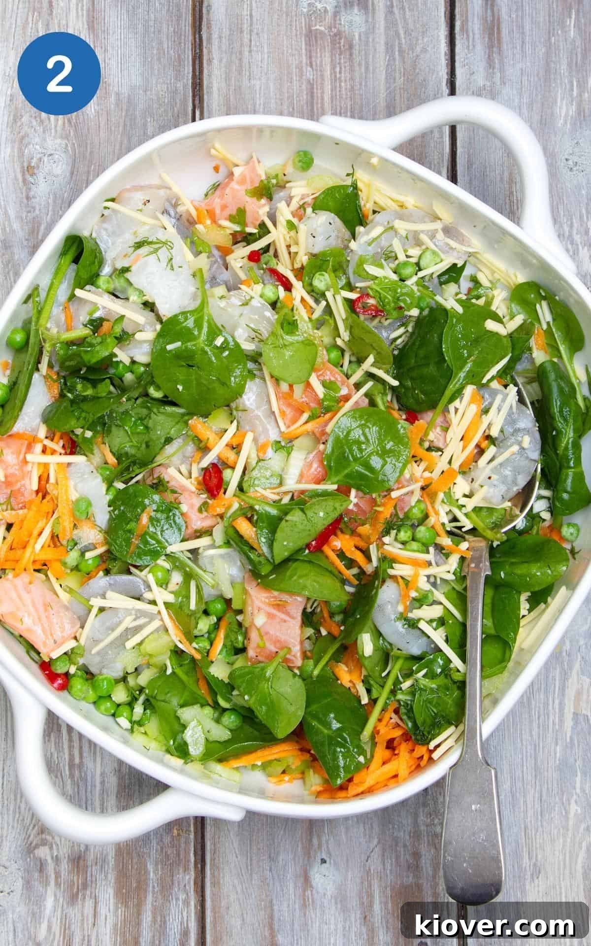 All the vibrant ingredients for the fish pie base, including various fish, vegetables, and herbs, expertly mixed together in a large baking dish, resting on a rustic wooden table.