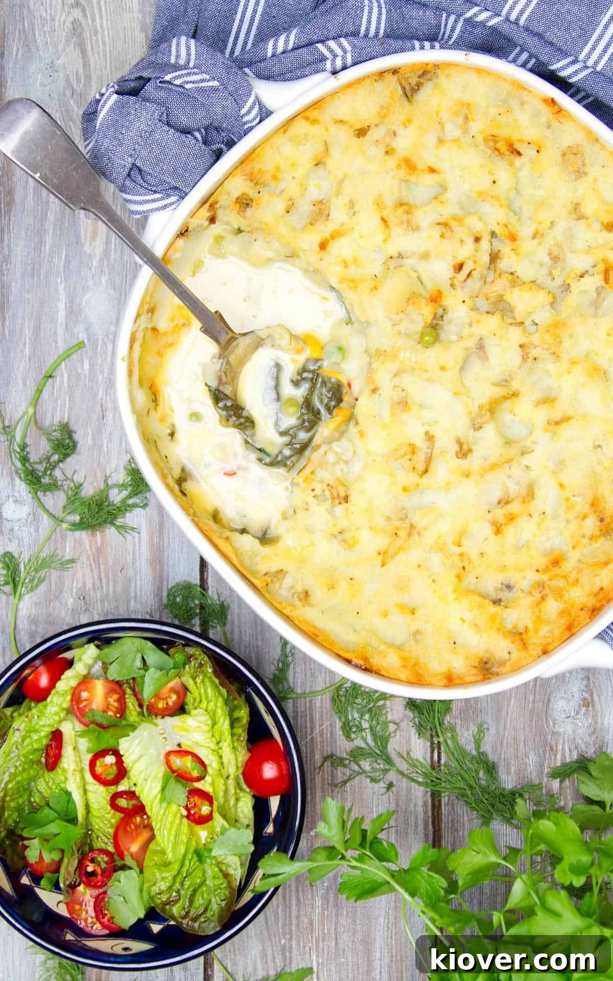 A large, inviting fish pie in a rustic baking dish, accompanied by a fresh green salad. Decorative herbs are thoughtfully placed around the plates, enhancing the aesthetic appeal of this wholesome and satisfying meal.