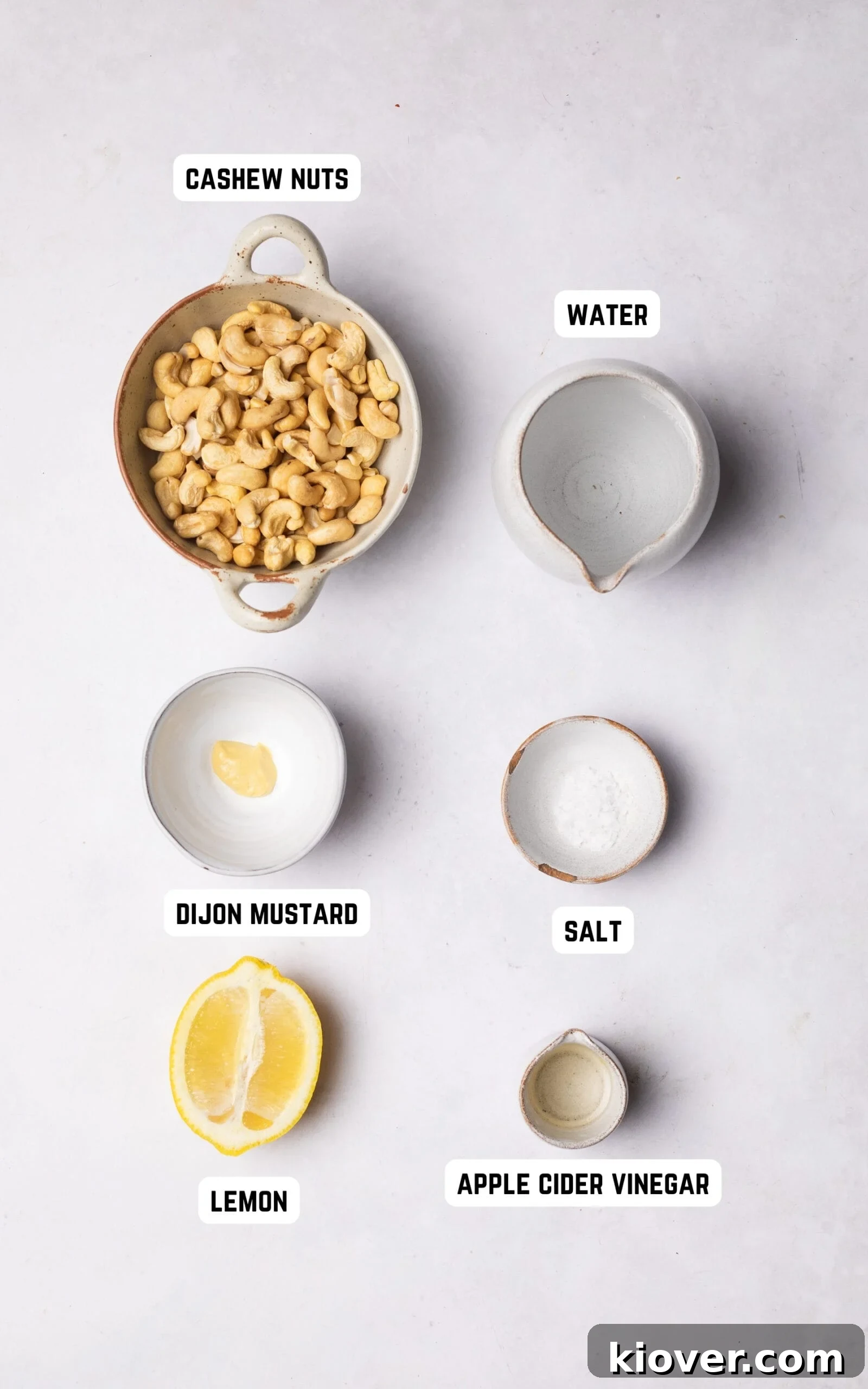 Creamy Vegan Sour Cream 3 All six ingredients laid out on a clean surface to make Vegan Sour Cream: cashew nuts, lemon, apple cider vinegar, Dijon mustard, salt, and water.
