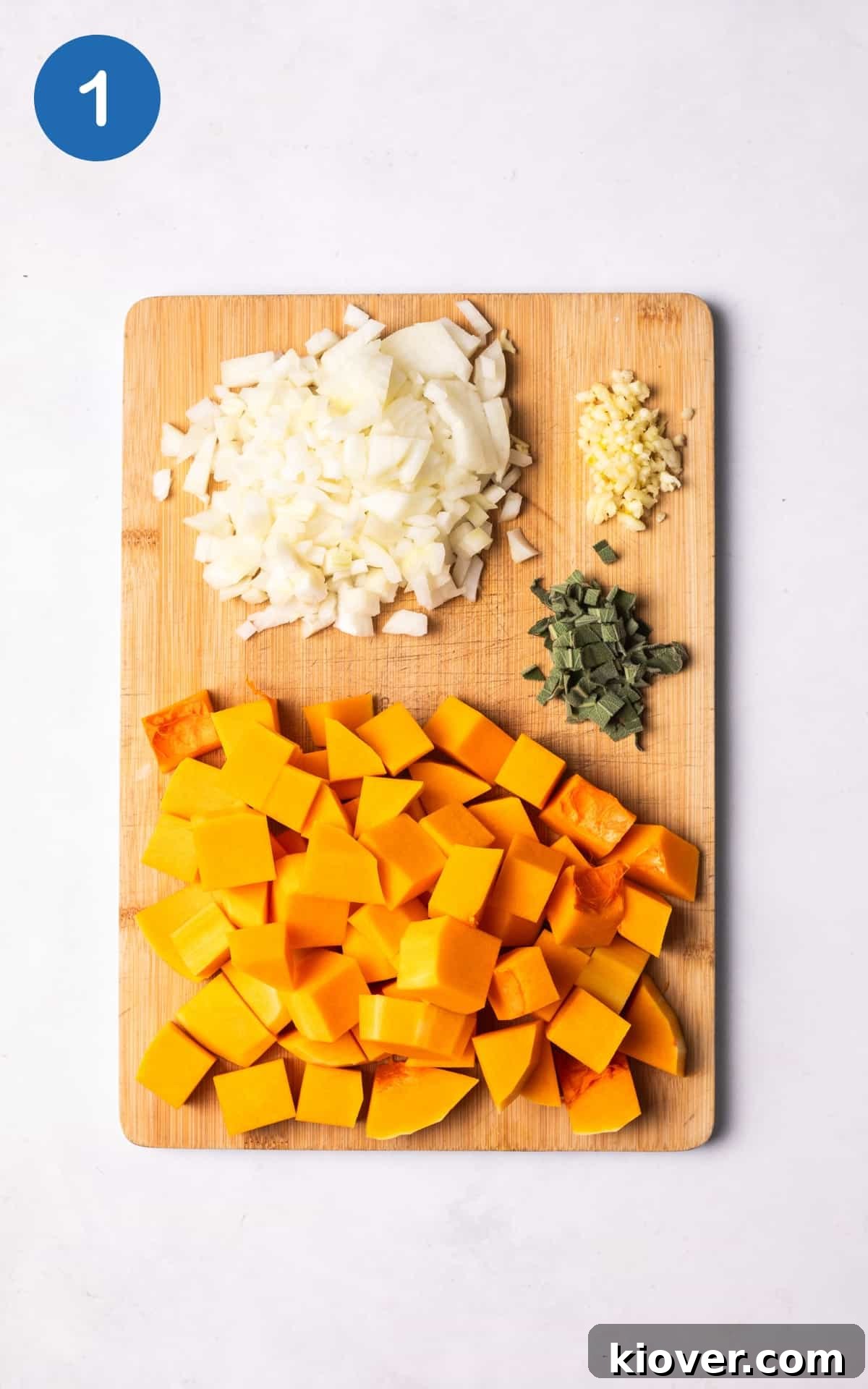 Autumn Squash Comfort 4 Peeled and cubed butternut squash, diced onion, and crushed garlic arranged on a wooden cutting board.