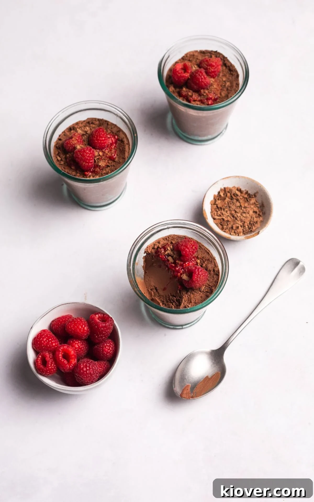 Beautifully presented vegan chocolate mousse in glass cups, topped with chocolate shavings and fresh raspberries, ready to be enjoyed.