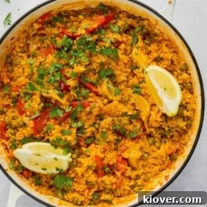 Overhead shot of vibrant vegetarian paella in a large white pan, garnished with fresh herbs.