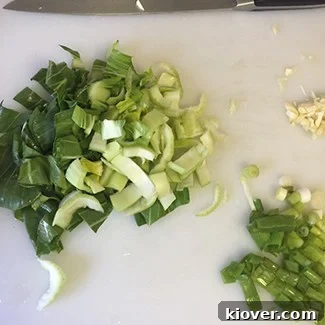 Beef Chow Mein: A Classic Stir-Fry Delight 3 Freshly chopped baby bok choy, vibrant green onions, and aromatic garlic on a cutting board, prepared for the Chow Mein.
