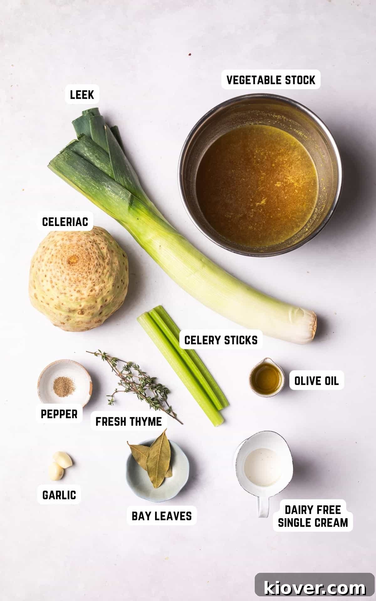 Fresh ingredients laid out on a wooden board, including celeriac, leeks, garlic cloves, celery sticks, bay leaves, and fresh thyme, prepared for making celeriac soup.
