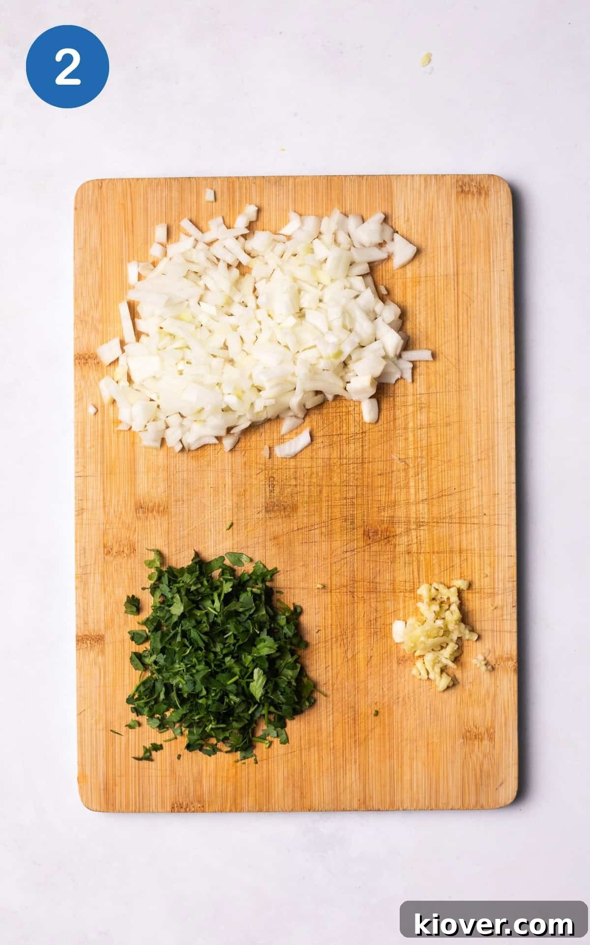 Crispy Zucchini Fritters 5 Finely diced onion, chopped parsley, and crushed garlic ready on a wooden cutting board.