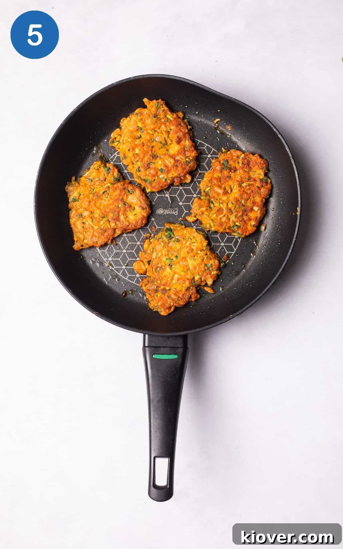 Crispy Zucchini Fritters 8 Courgette fritters frying in a hot pan, sizzling and turning golden brown.