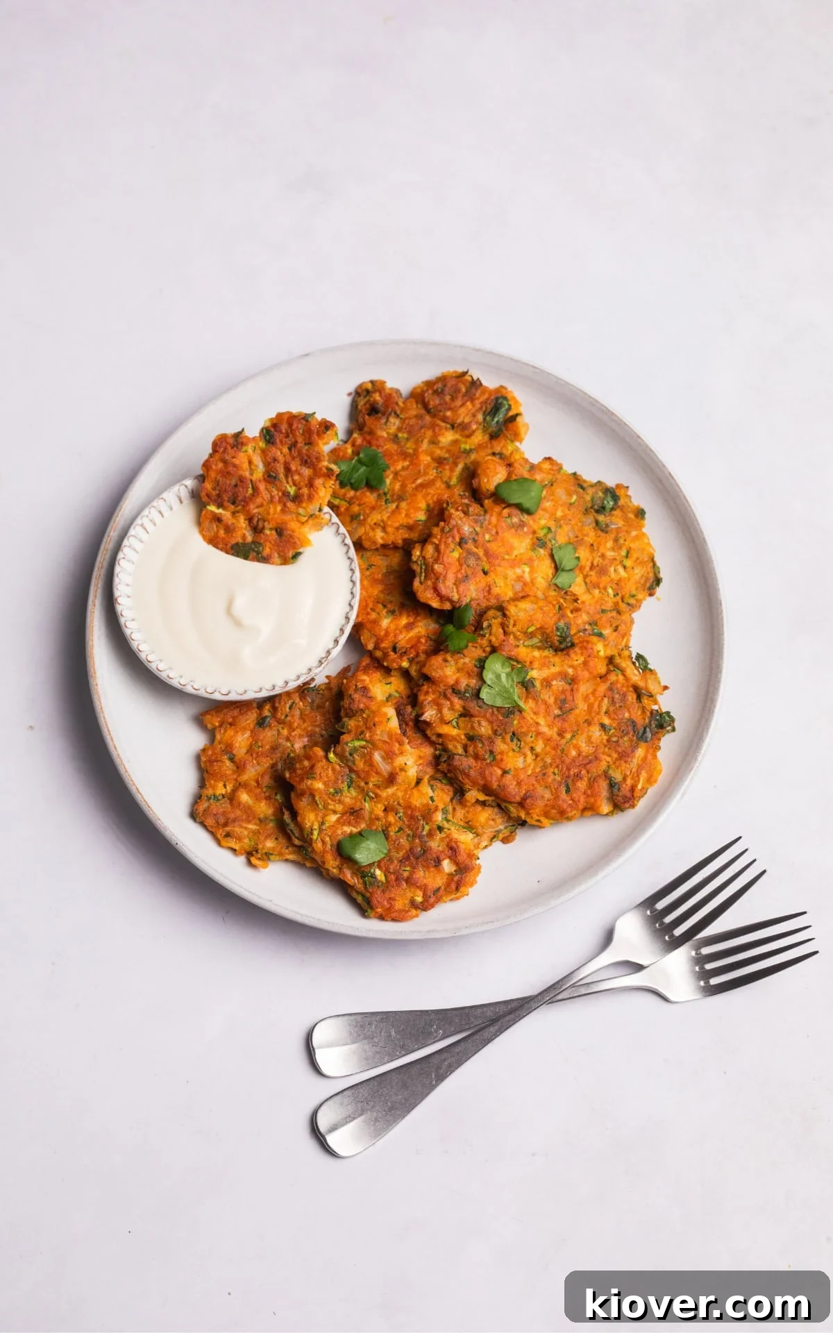 Crispy Zucchini Fritters 10 Plated zucchini fritters accompanied by a small bowl of coconut yogurt for dipping.