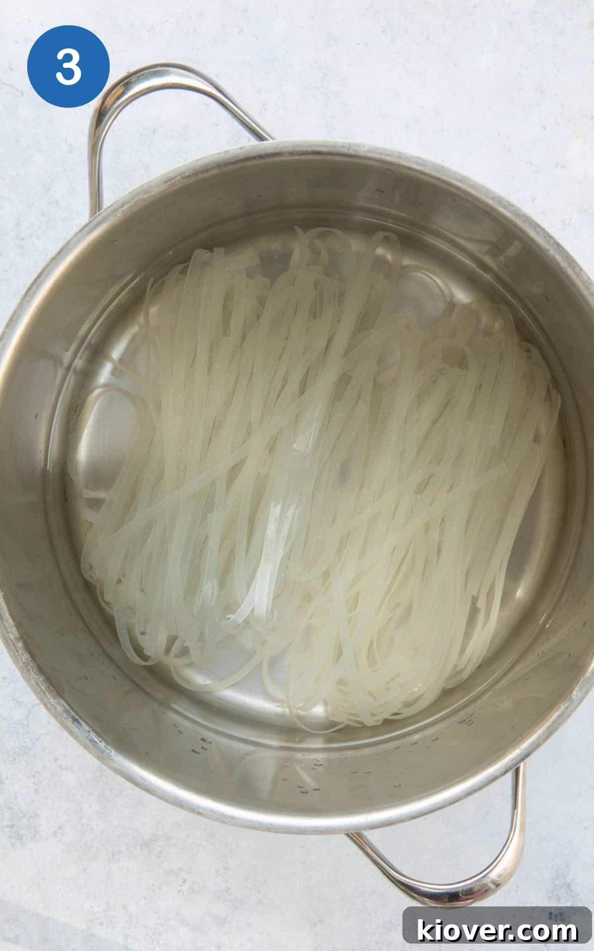 Rice noodles boiling in a pot of water.