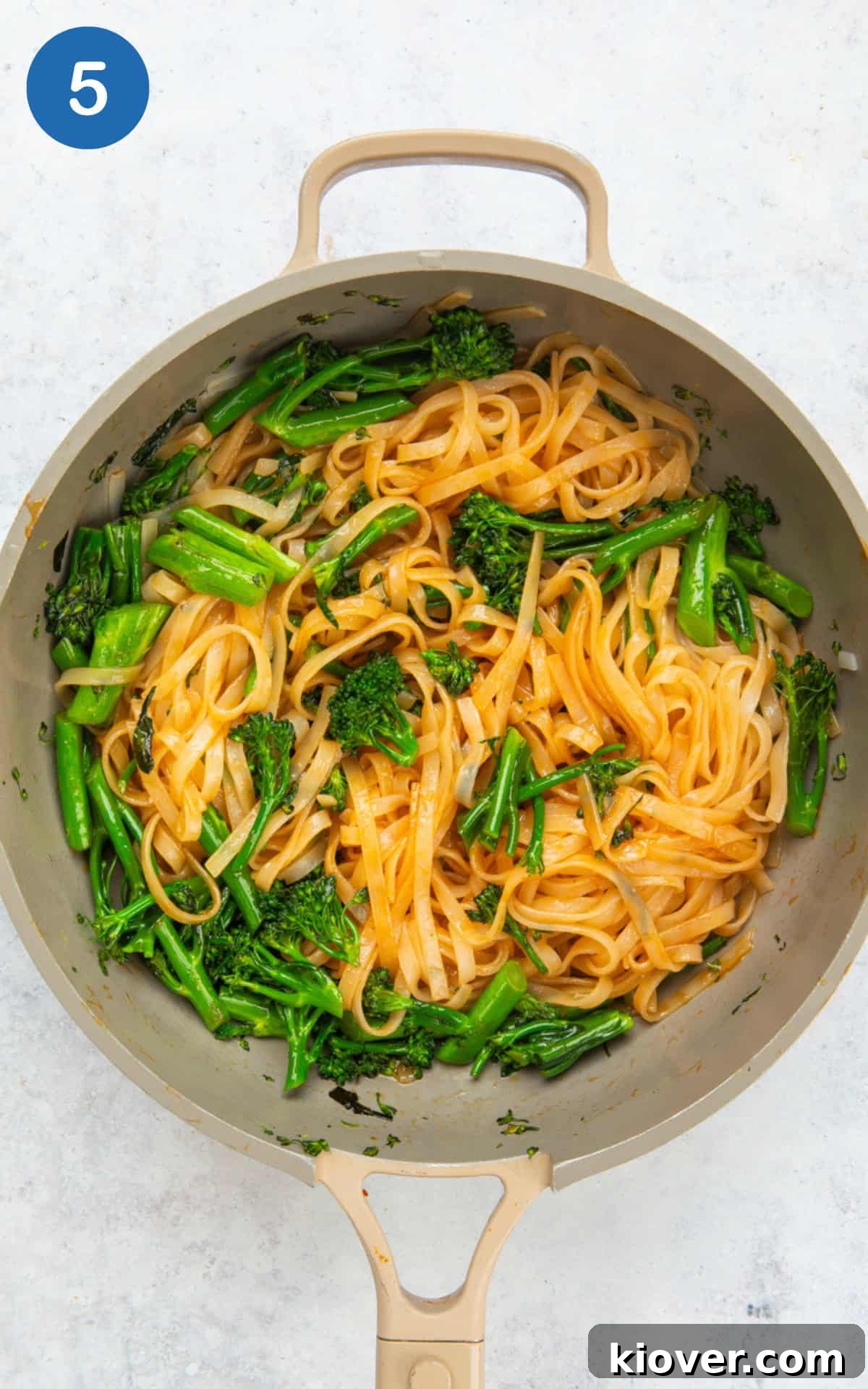 Drained noodles, teriyaki sauce, and broccoli being stirred in a pan.