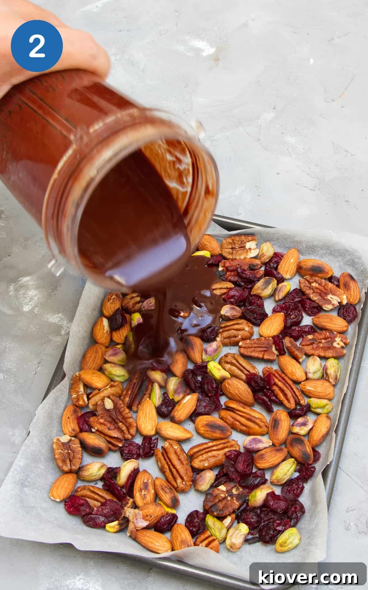 Plant-Based Rocky Road Delights 5 Pouring melted chocolate mixture over a tray of nuts and fruit.