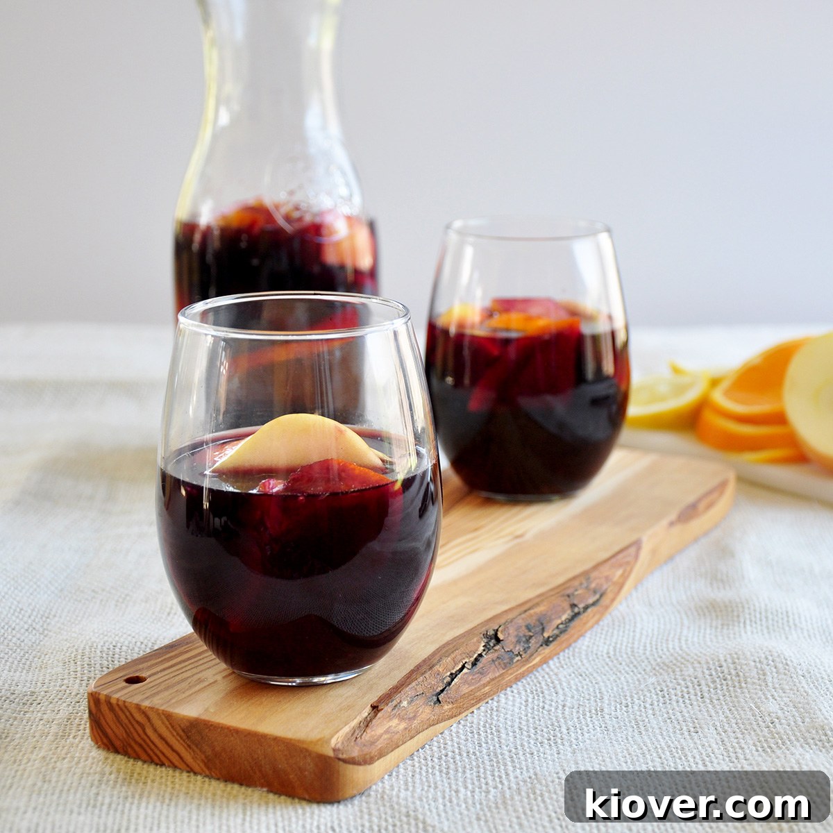 Red Sangria Serving Suggestion Side view of two glasses of red sangria with a carafe of sangria in the background, garnished with fruit.
