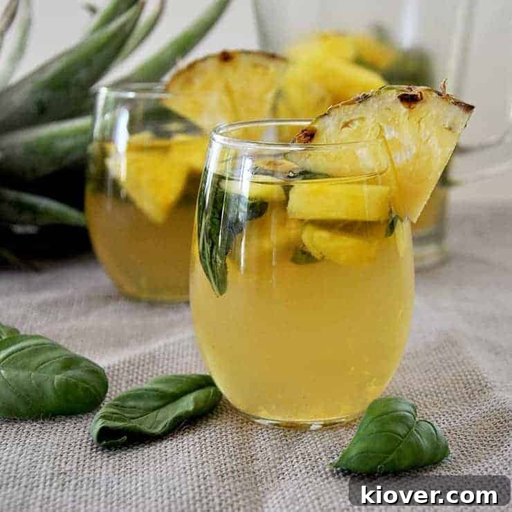 Finished Sangria Side Shot Two glasses of basil pineapple moscato sangria with some basil laying on a mat and pineapple head in the background