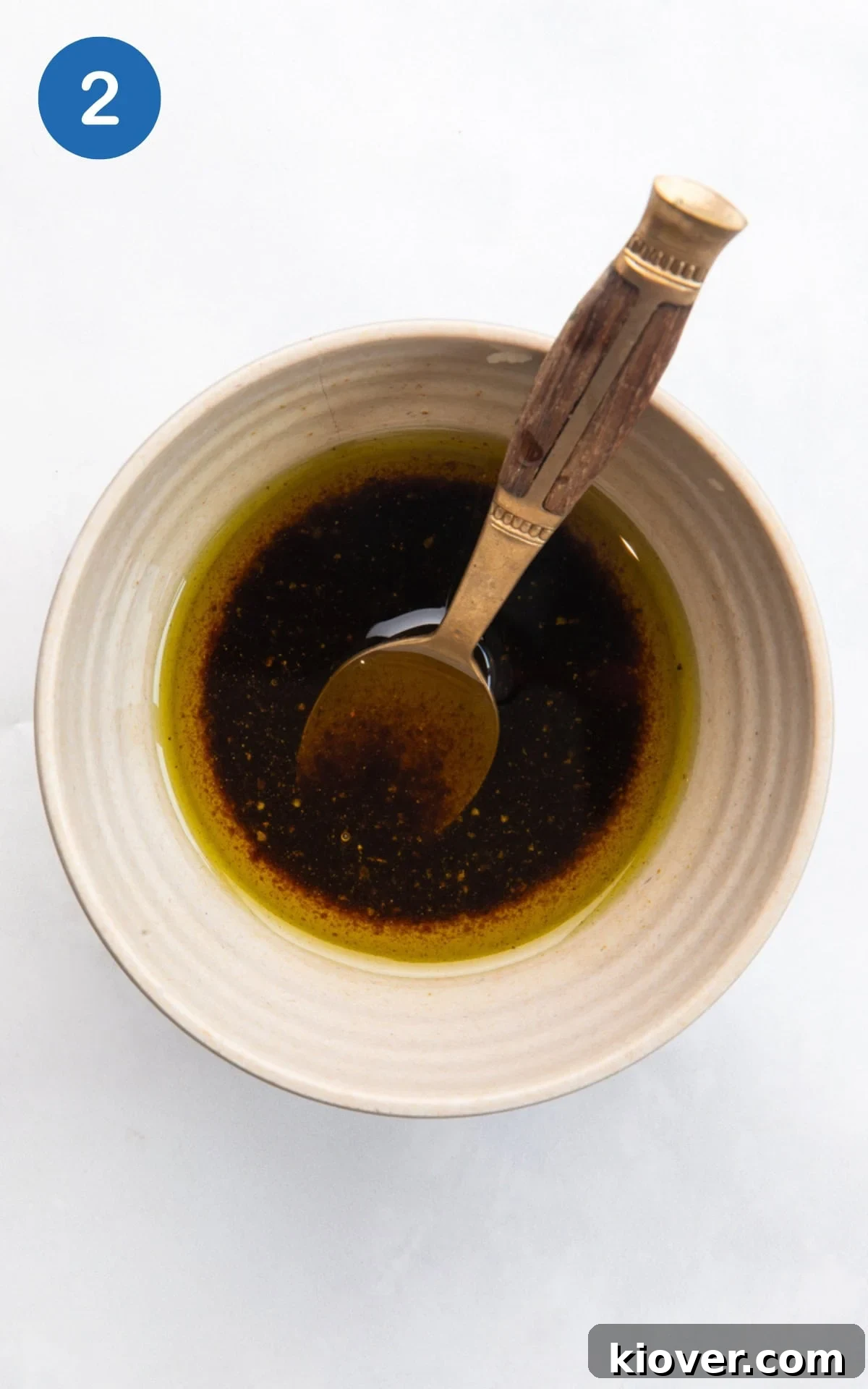 A small bowl containing extra virgin olive oil, balsamic vinegar, and a pinch of salt and pepper, being whisked together.