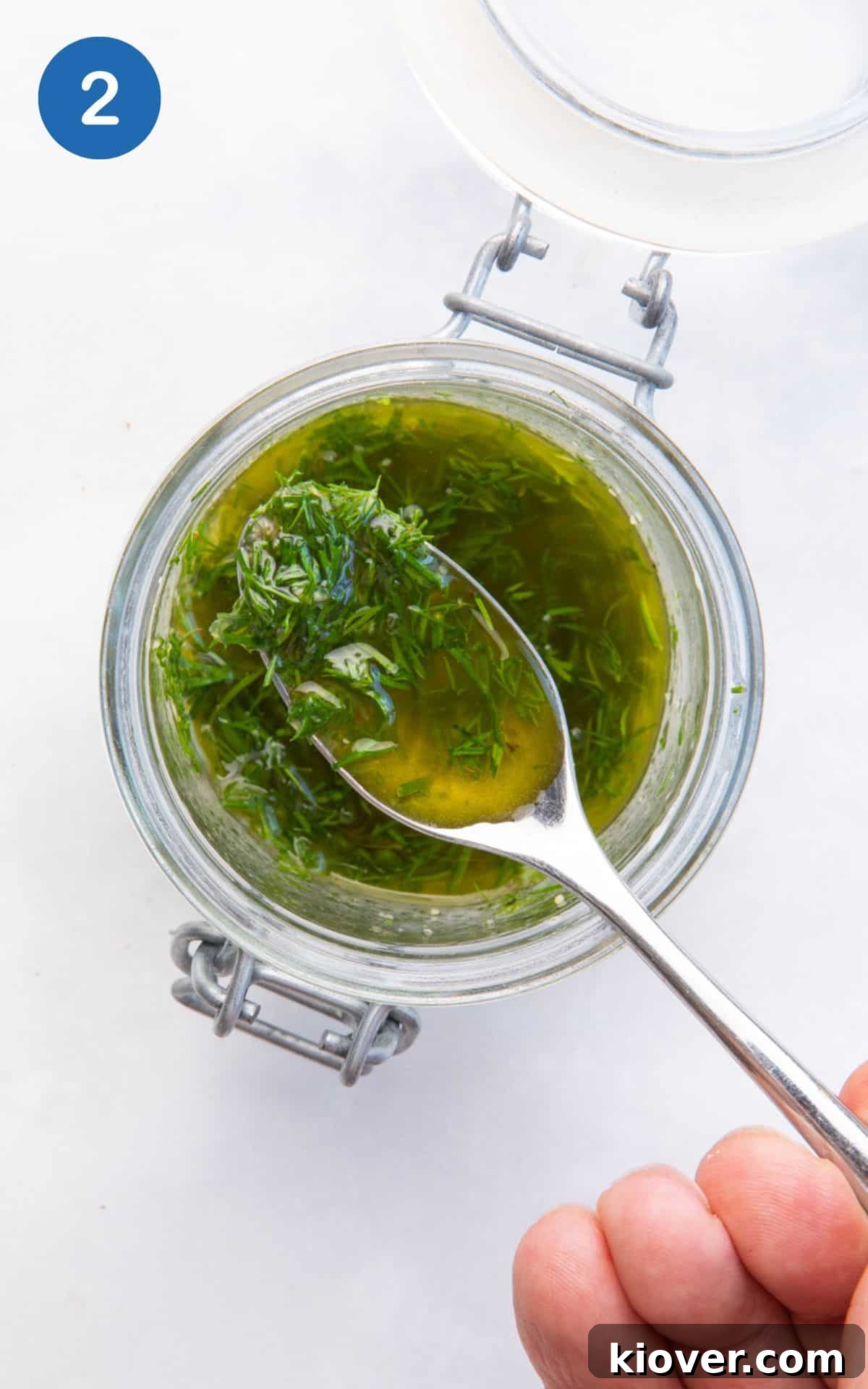A glass jar containing olive oil, cider vinegar, garlic powder, and fresh dill, ready to be mixed for the dressing.
