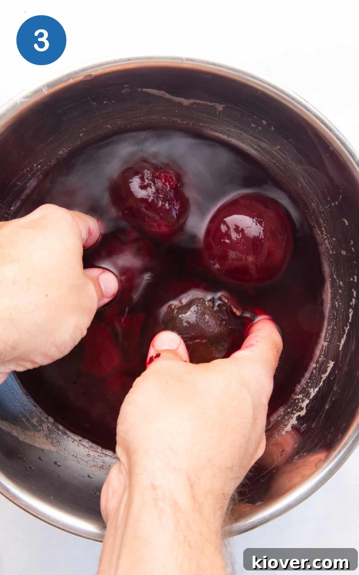 Hands easily removing the skin from a cooked beetroot after cooling.