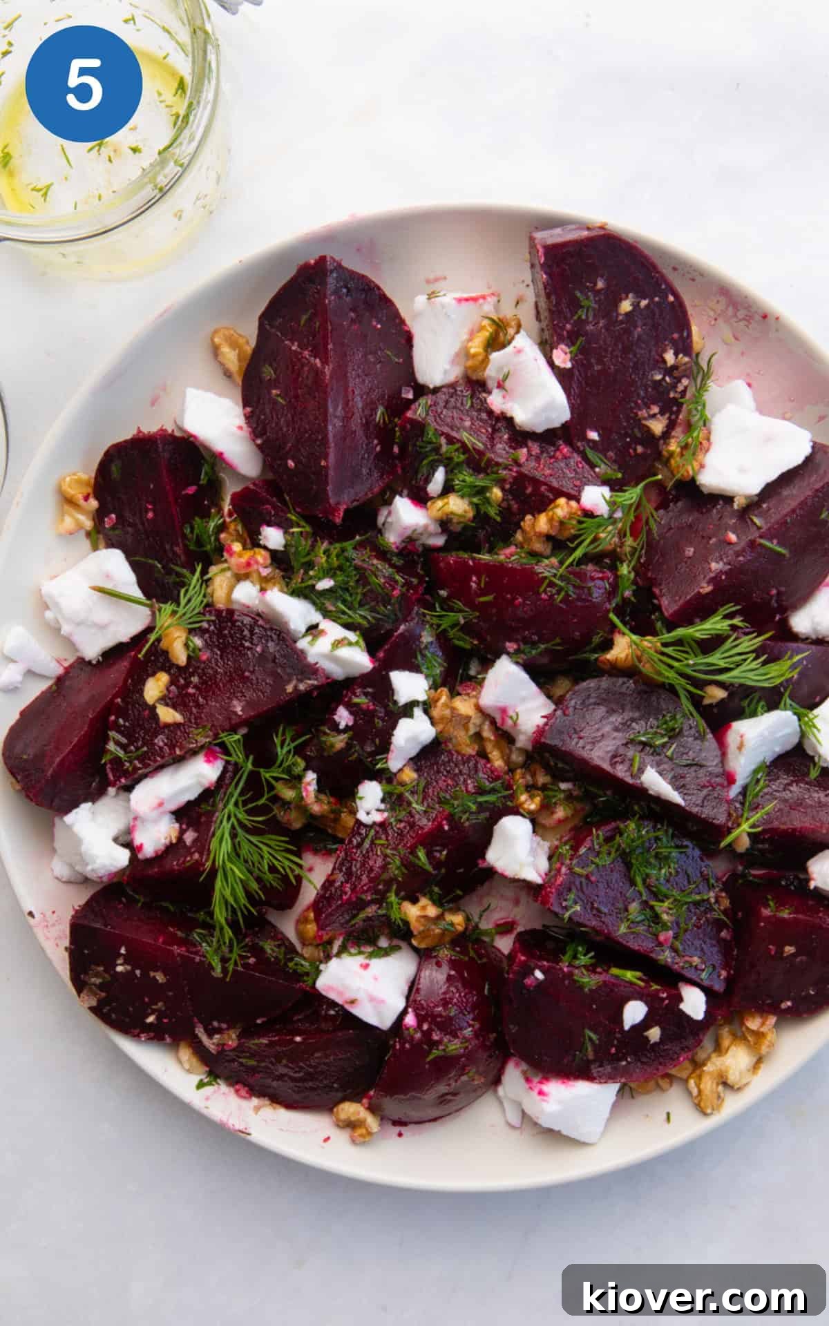 A large salad bowl filled with quartered beetroot, walnuts, and drizzled with dill dressing, ready for tossing.