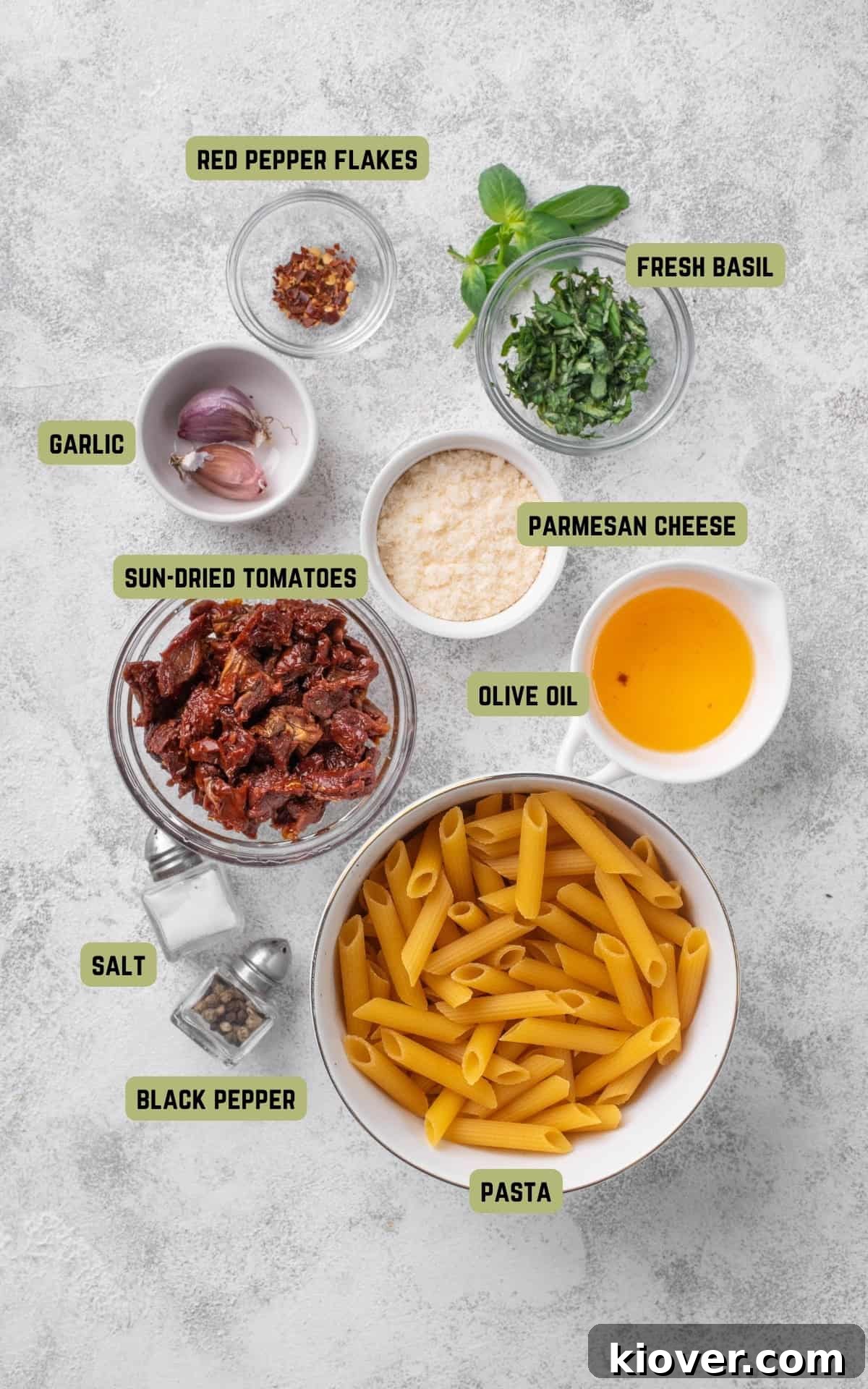 A flat lay photograph showcasing all the fresh ingredients needed to make Sun Dried Tomato Pasta, including pasta, sun-dried tomatoes, garlic, olive oil, basil, and Parmesan cheese.