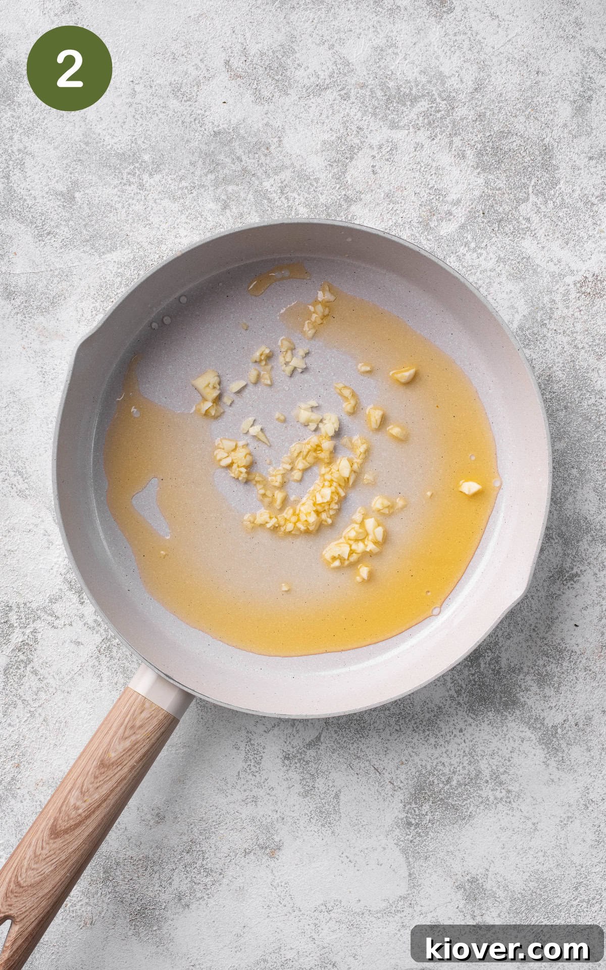 Minced garlic being gently fried in olive oil in a large skillet, releasing its fragrant aroma.