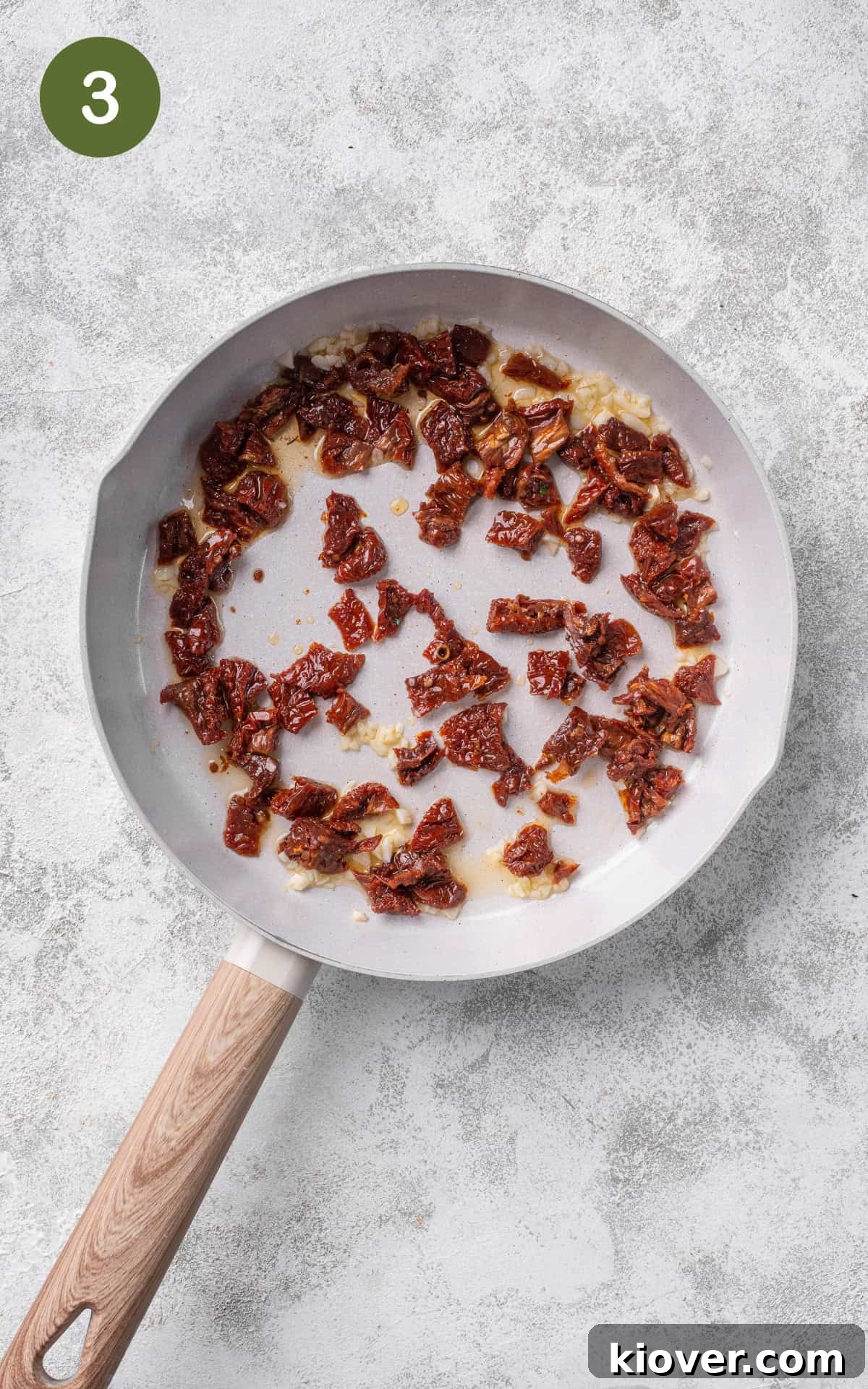 Chopped sun-dried tomatoes being cooked in a pan with sautéed garlic and olive oil.