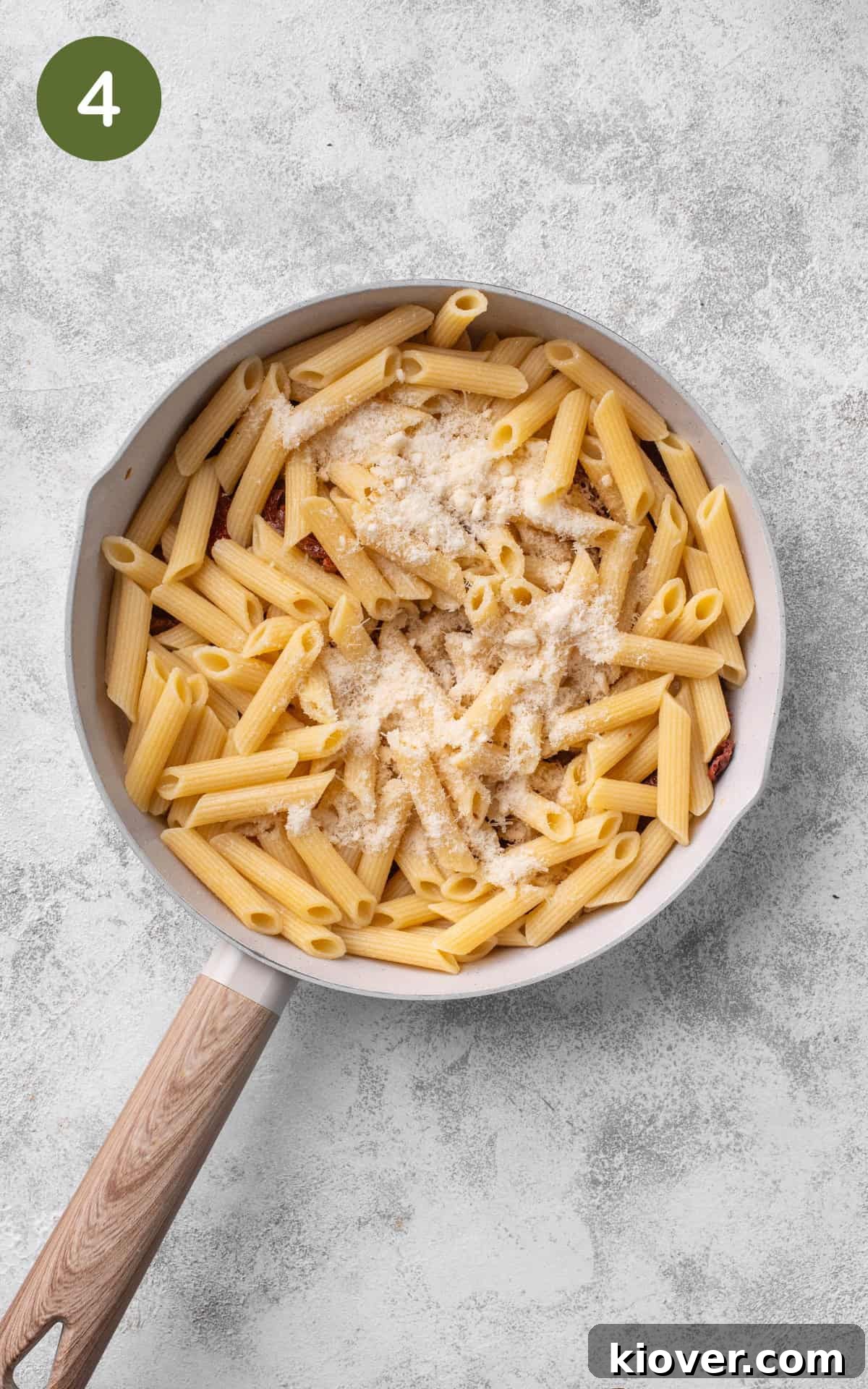Cooked pasta being added to the skillet with the sun-dried tomato and garlic mixture, ready to be tossed with grated Parmesan cheese.