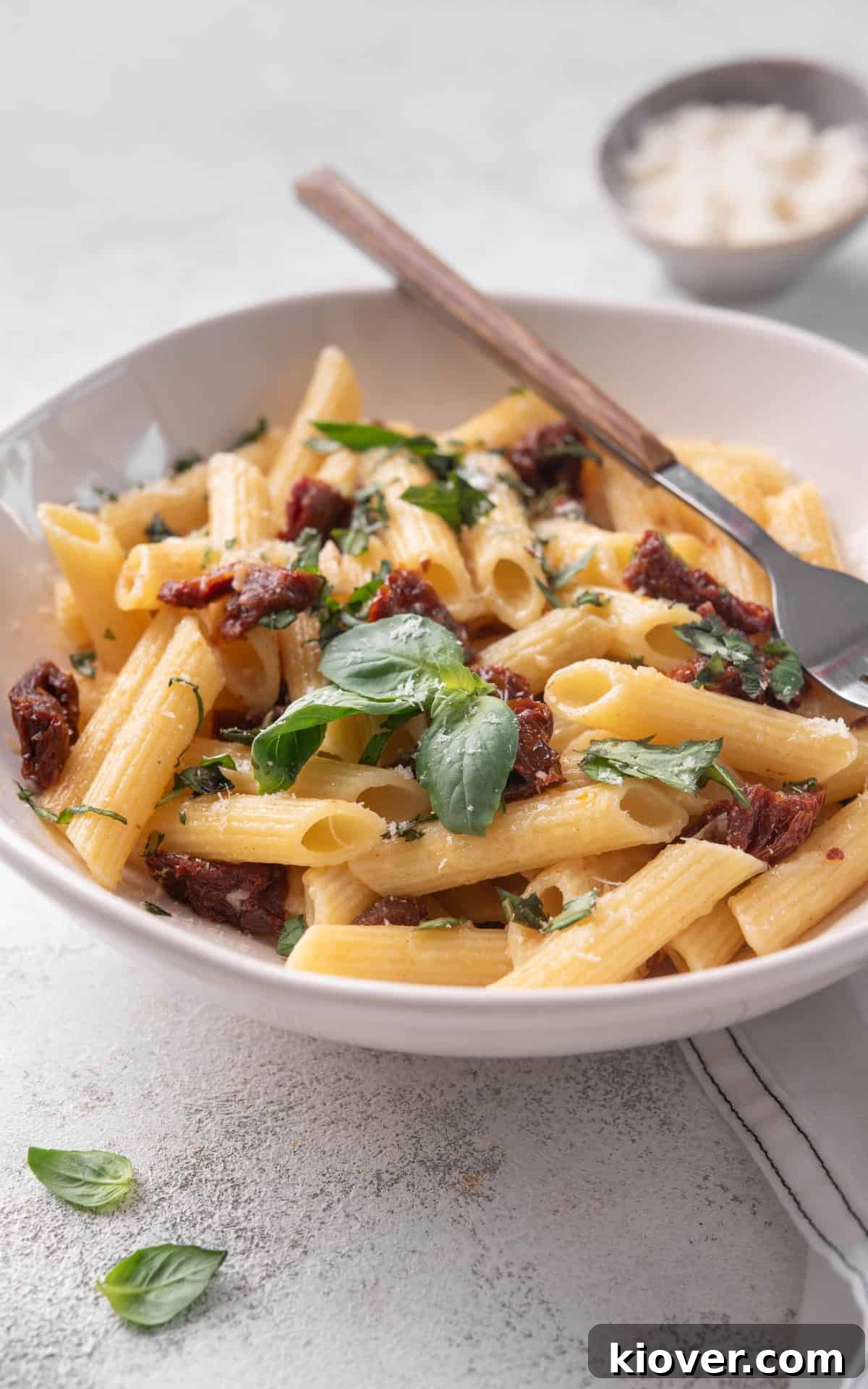 A close-up shot of Sun Dried Tomato Pasta served in a bowl, garnished with fresh basil leaves and grated Parmesan cheese, highlighting its vibrant colors and inviting texture.