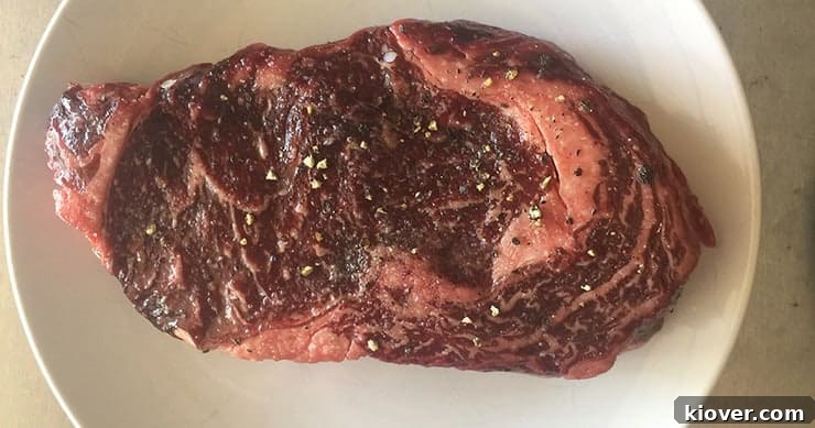 An uncooked, generously marbled ribeye steak resting on a clean cutting board, ready for seasoning and grilling.