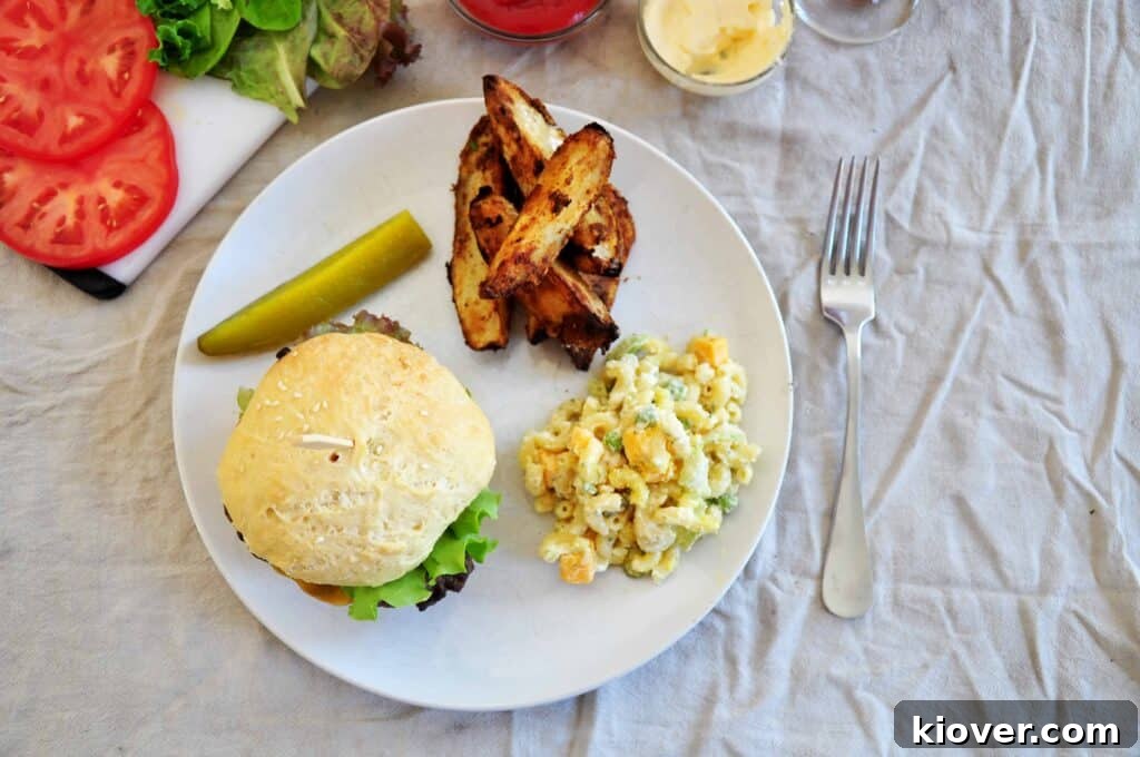 An overhead shot of a gourmet grilled sirloin burger, perfectly topped with melted cheese, served alongside macaroni salad, crispy jojos, a zesty pickle, and fresh tomatoes.