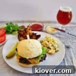 A plate featuring a sirloin burger, a Surly Furious beer, macaroni salad, and some jojos
