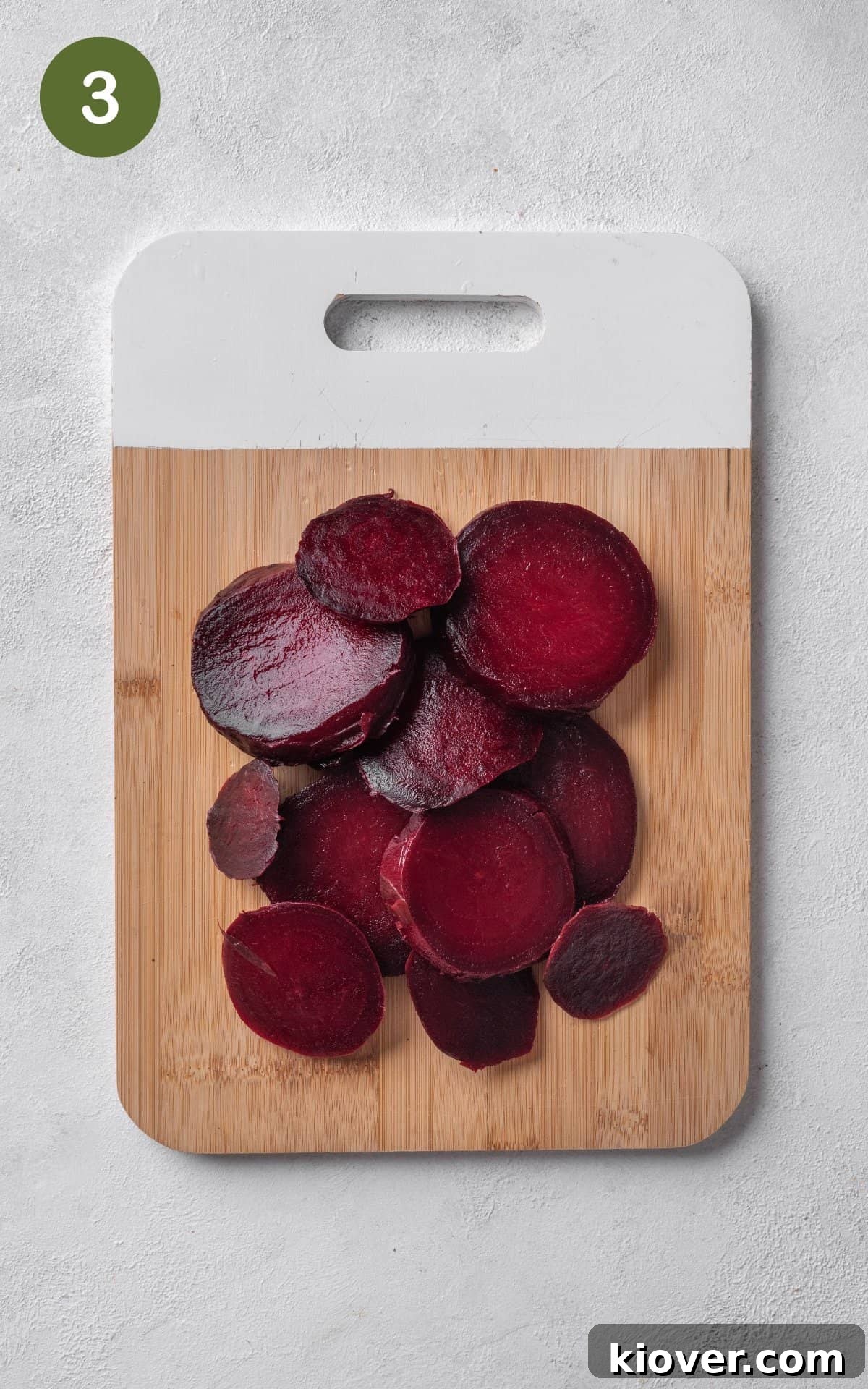 Slices of cooked and peeled beets neatly arranged on a wooden cutting board, ready for jarring.