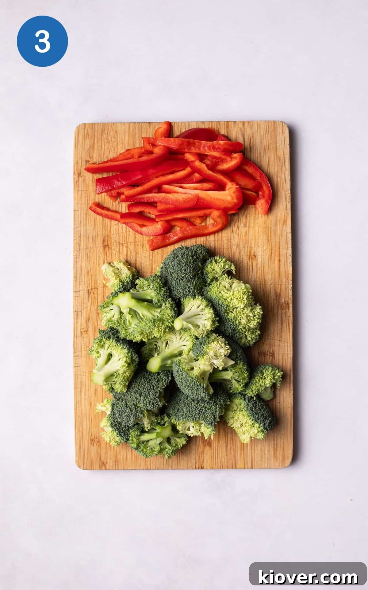 Chopped broccoli florets and sliced red bell pepper on a wooden cutting board.
