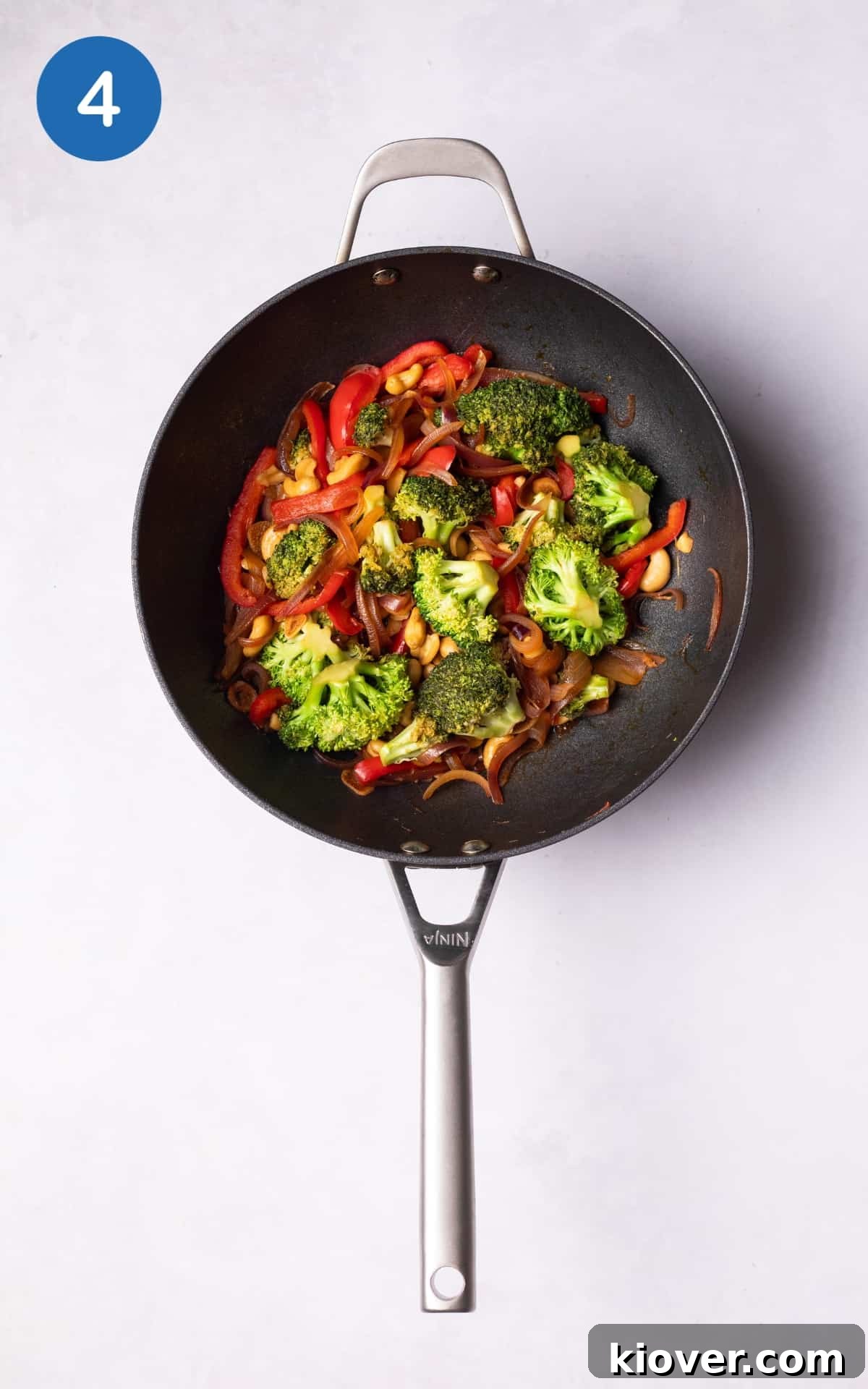 Broccoli florets, red pepper strips, and cashews cooking in a wok with the flavorful sauce.