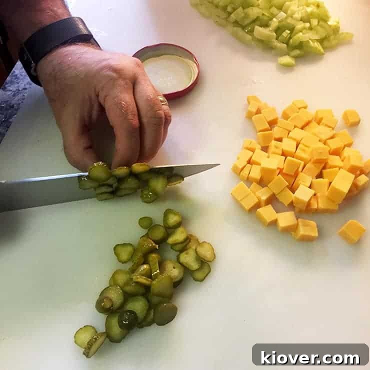 Chopping Pickles cutting board with ben myhre chopping pickles. There is diced cheese and chopped celery on the same chopping board.