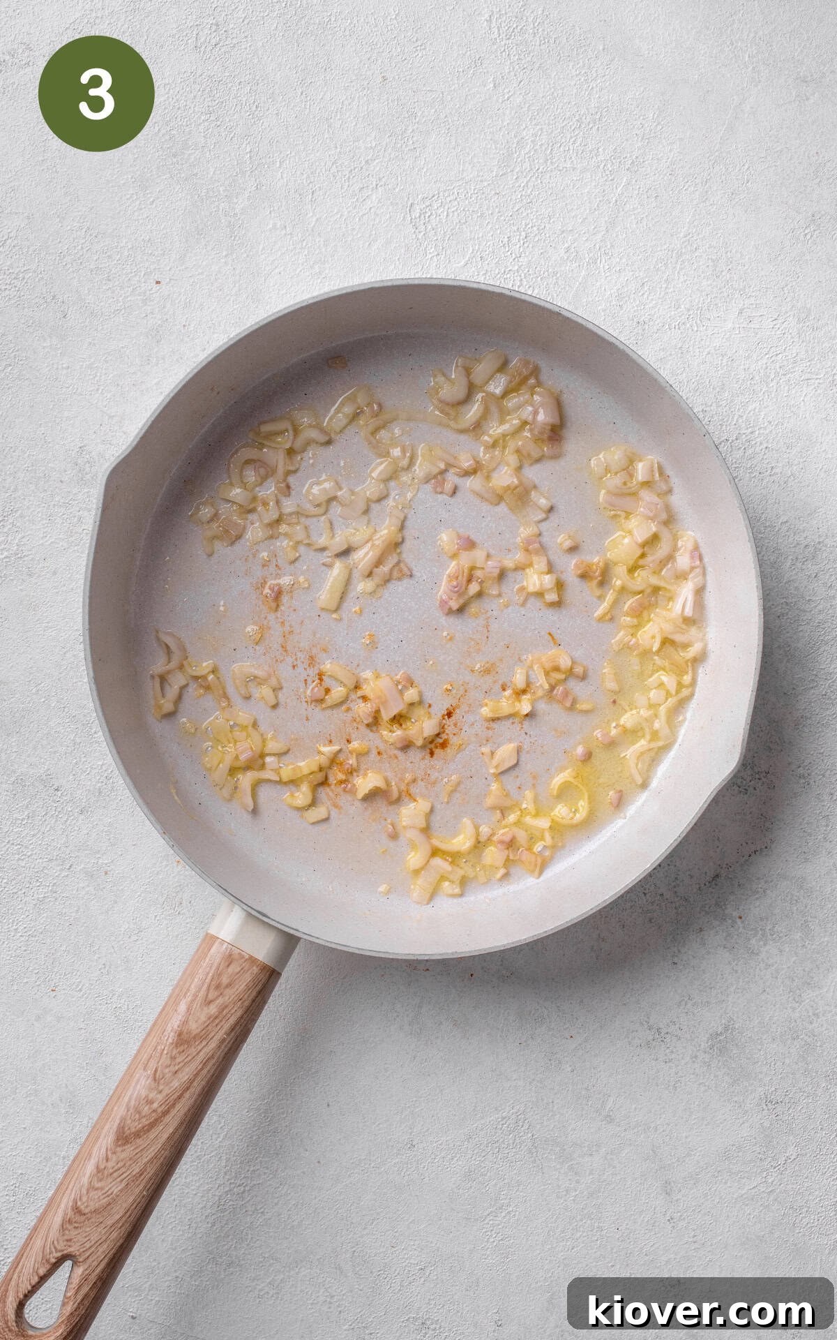 Finely chopped shallots and crushed garlic cooking in a pan, becoming fragrant.